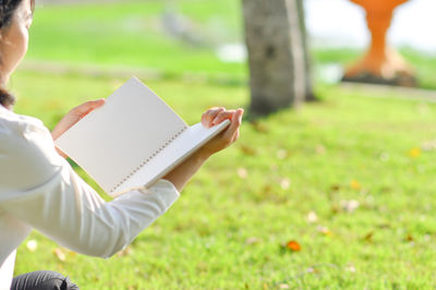 Midsection of woman reading book on field