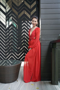 Portrait of young woman standing against red wall