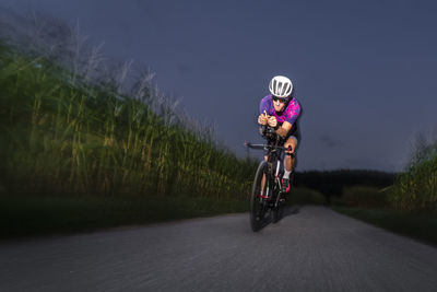 Athlete riding racing bicycle on road at dusk