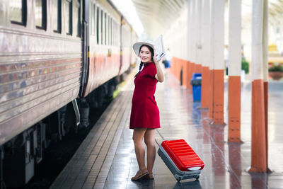 Portrait of smiling woman with suitcase walking by train at railroad station platform