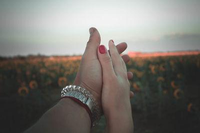 Midsection of woman hand on field against sky during sunset