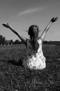 Rear view of girl with arms raised sitting on grassy field