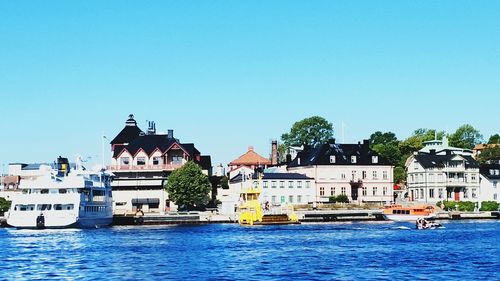 Buildings by river against clear blue sky