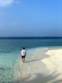 Rear view of man walking on shore at beach against sky