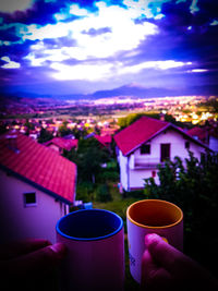 Close-up of hand holding coffee cup by house against sky