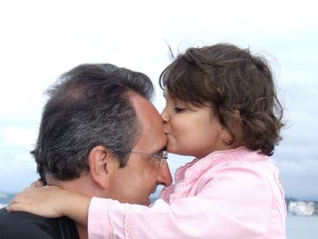 Close-up of girl kissing grandfather against cloudy sky