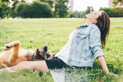 Side view of young woman holding dog on field