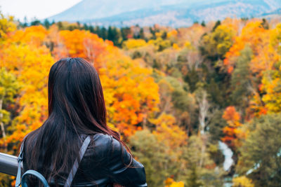 Rear view of woman standing by trees during autumn