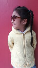 Cute girl wearing sunglasses while standing against pink wall