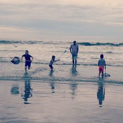 Children playing on beach against sky during sunset