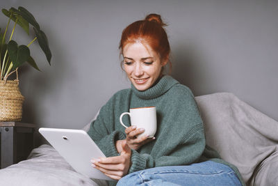 Young woman using mobile phone while sitting on bed at home