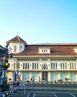 People on road by buildings against clear blue sky