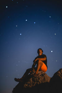 Low angle view of young woman sitting on rock