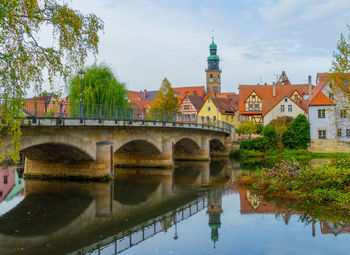 Arch bridge over river by buildings against sky