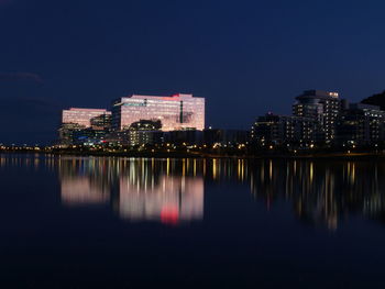 Illuminated buildings by lake against sky in city at night