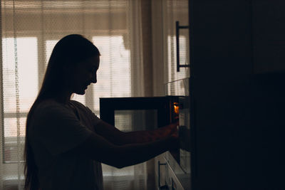 Side view of woman looking through window