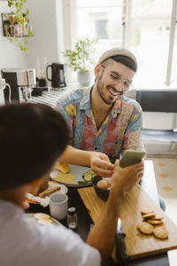 Man sharing smart phone with boyfriend while having food at home