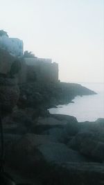 View of rocky coastline against clear sky during foggy weather