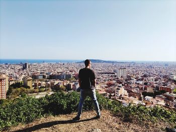 Rear view of man looking at cityscape against sky