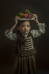 Cute girl holding fruits against black background