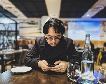 Front view of young asian man using mobile phone at table in restaurant.