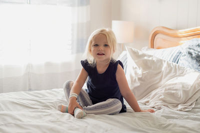 Full length portrait of girl sitting on bed at home