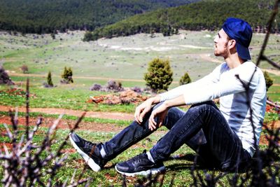 Side view of young man sitting on land