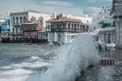 Sea waves splashing on shore against buildings in city