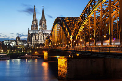 Illuminated hohenzollern bridge over river rhine by cologne cathedral at dusk