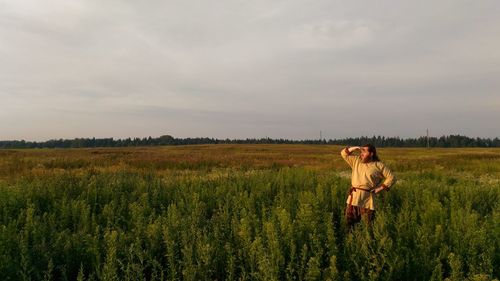 Man standing amidst plants on field against cloudy sky during sunset