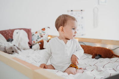 Cute girl looking away sitting on bed at home