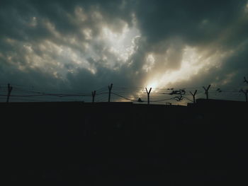 Low angle view of silhouette electricity pylon against storm clouds