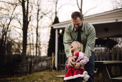 Happy father tickling daughter while standing at yard