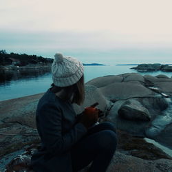 Side view of woman having coffee while sitting at lakeshore during sunset