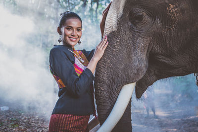 Portrait of smiling woman standing with elephant in forest