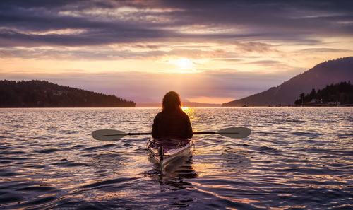 Rear view of man on sea against sky during sunset