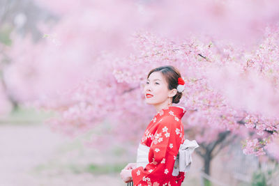 Side view of woman against pink cherry blossom trees