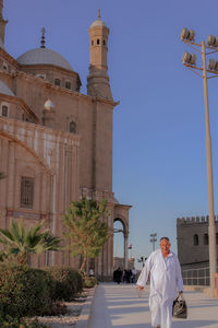 Man walking on footpath against mosque