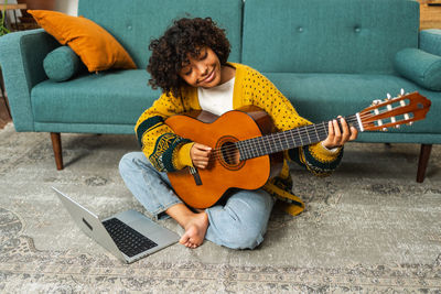 Young woman playing guitar while sitting on sofa at home