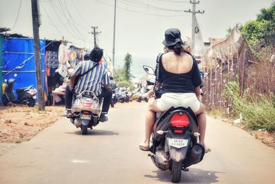 Rear view of man riding motor scooter on road