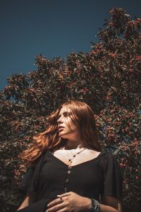 Low angle view of woman standing by tree against sky