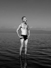 Shirtless man standing in sea against sky