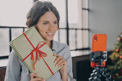 Cheerful woman holding gift box vlogging at home