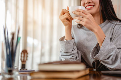 Midsection of woman sitting with cup at desk