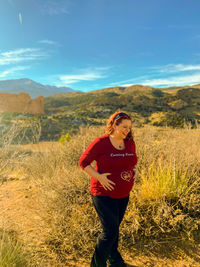 Smiling pregnant woman standing on field against sky