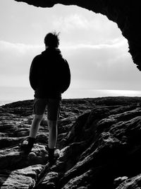 Rear view of teenage boy standing on rock against sea at beach