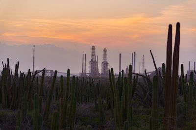 Silhouette factory against cloudy sky during sunset