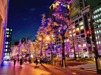 Illuminated city street by buildings at night