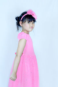 Cute girl looking away while standing against pink background