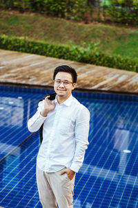 Portrait of young man standing by swimming pool